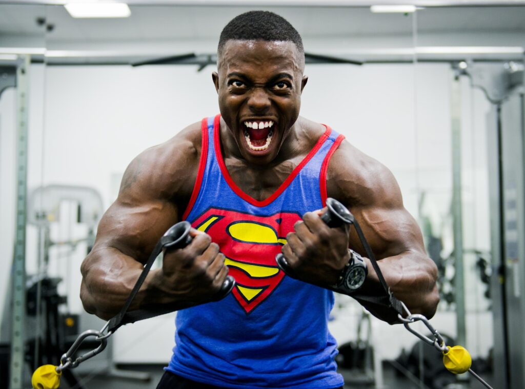 A man in a superman tank top showcasing hypertrophy gains in a gym.
